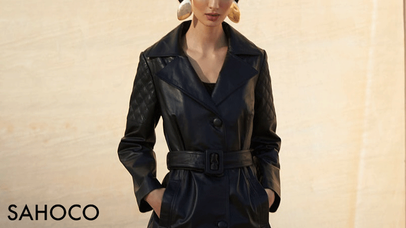 Casaco de pele (trench coat) da marca portuguesa SAHOCO. Este modelo específico caracteriza-se pelo seu efeito de pele preta, gola de lapela e um cinto largo coordenado com fivela retangular.