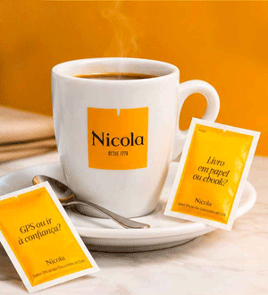 Chávena de café da marca portuguesa CAFÉ NICOLA® acompanhada por pacotes de açúcar com mensagens, sobre fundo em tons de laranja.