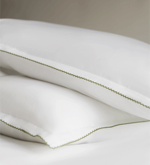Almofadas brancas da marca portuguesa CTN TORRES NOVAS EST. 1845®, com acabamento decorativo verde, apresentadas sobre roupa de cama branca.
