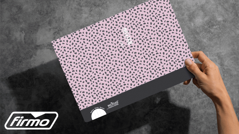 Uma mão segura uma pasta de arquivo rosa com padrão preto e faixa preta na base, sobre um fundo cinzento texturado. O logótipo branco da marca portuguesa FIRMO® surge no canto inferior esquerdo.