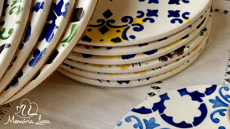 Pratos de cerâmica pintados à mão pela marca portuguesa Memória Lusa. Cada peça é única, com ligeiras variações que refletem o trabalho manual.