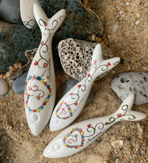 Sardinhas de cerâmica pintadas à mão pela marca portuguesa Memória Lusa, com motivos que lembram os lenços dos namorados. Cada peça é única, com ligeiras variações que refletem o trabalho manual.