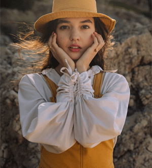 Modelo com chapéu e conjunto em tons de branco e mostarda da marca portuguesa SIZ®, fotografada num cenário rochoso ao ar livre.