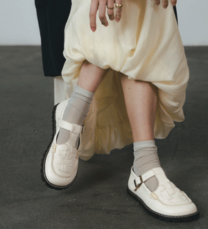 Sapatos barefoot brancos da marca portuguesa URZE BAREFOOT LABEL® com fivela lateral e detalhe entrançado, combinados com meias e vestido em tons claros.