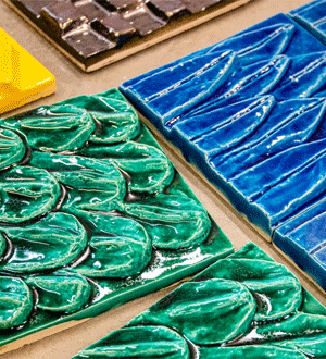 Azulejos cerâmicos da marca portuguesa VIÚVA LAMEGO® em tons de verde, azul, amarelo e castanho, com superfícies vidradas e relevos inspirados em formas orgânicas.