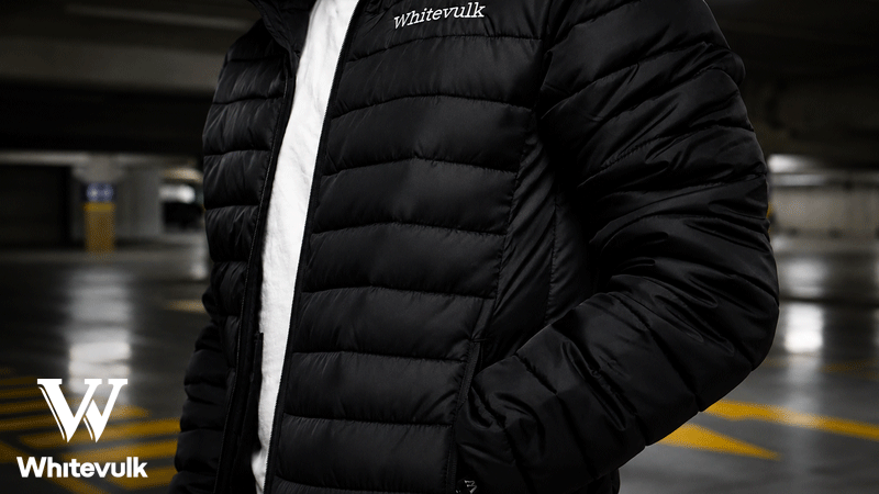 Casaco acolchoado preto da marca portuguesa WHITEVULK® com logótipo bordado no peito, fotografado num parque de estacionamento.